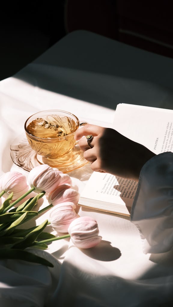 A serene moment with tea, tulips, and a book in natural light.